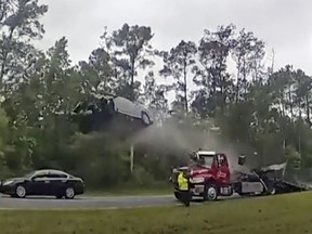 In this image taken from police body camera video provided by the Lowndes County, Ga., Sheriff's Office, a vehicle goes airborne after driving up the ramp of a flatbed tow truck on a Georgia highway, Wednesday, May 24, 2023, in Lowndes County, Ga. The Nissan Altima was launched 120 feet (37 meters) down the highway, according to a police report. The driver, a 21-year-old woman from Florida, was taken to South Georgia Medical Center with serious injuries. (Lowndes County Sheriff's Office via AP)