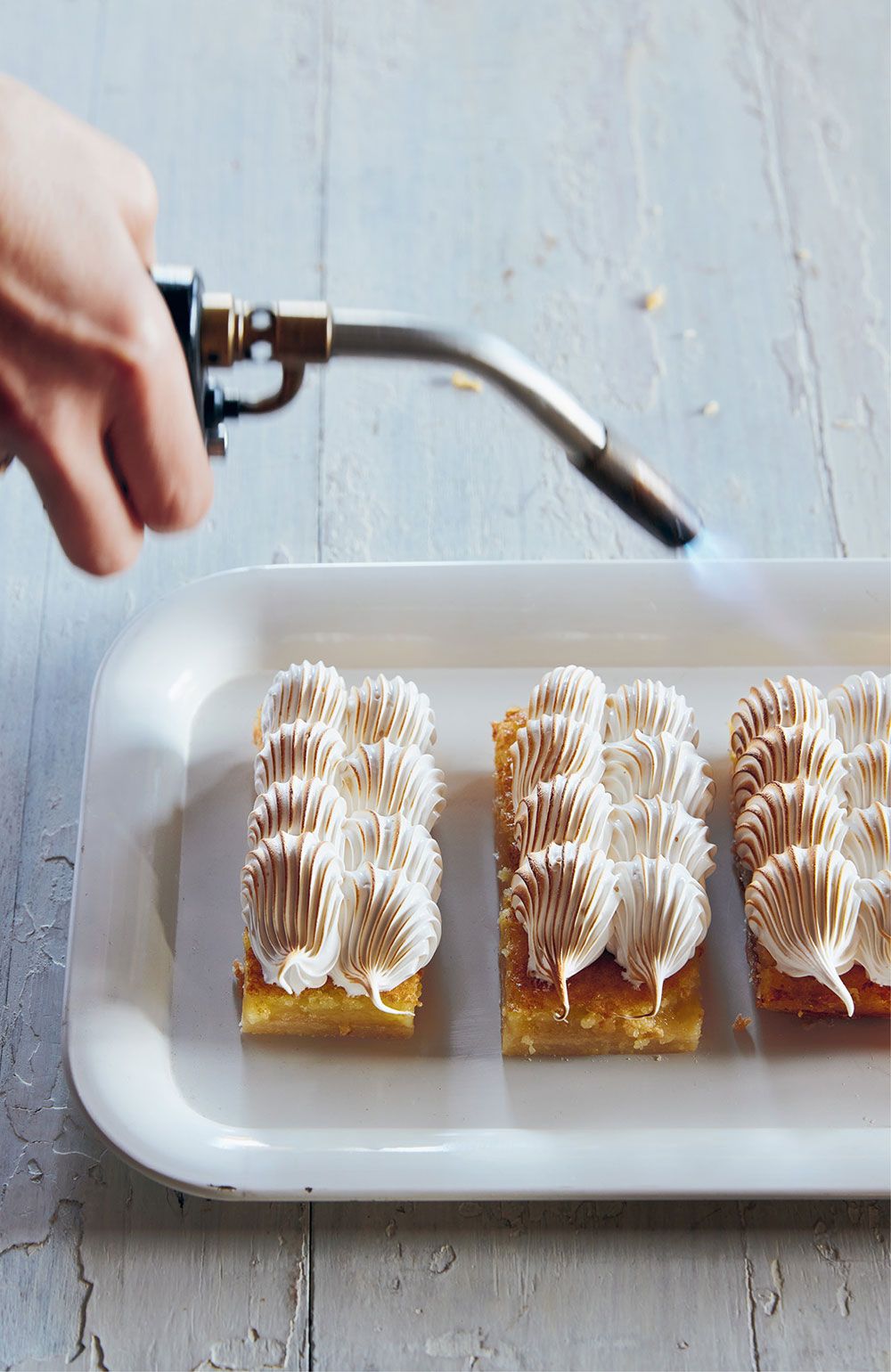 A person takes a kitchen blowtorch to lemon meringue pie bars