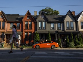A person walks by a row of houses in Toronto on Tuesday July 12, 2022. A new policy allowing single family homes to be converted into low-rise multiplexes in Toronto is being hailed by observers as a welcome move, although experts warn it won't make housing more affordable in Canada's most populous city right away.