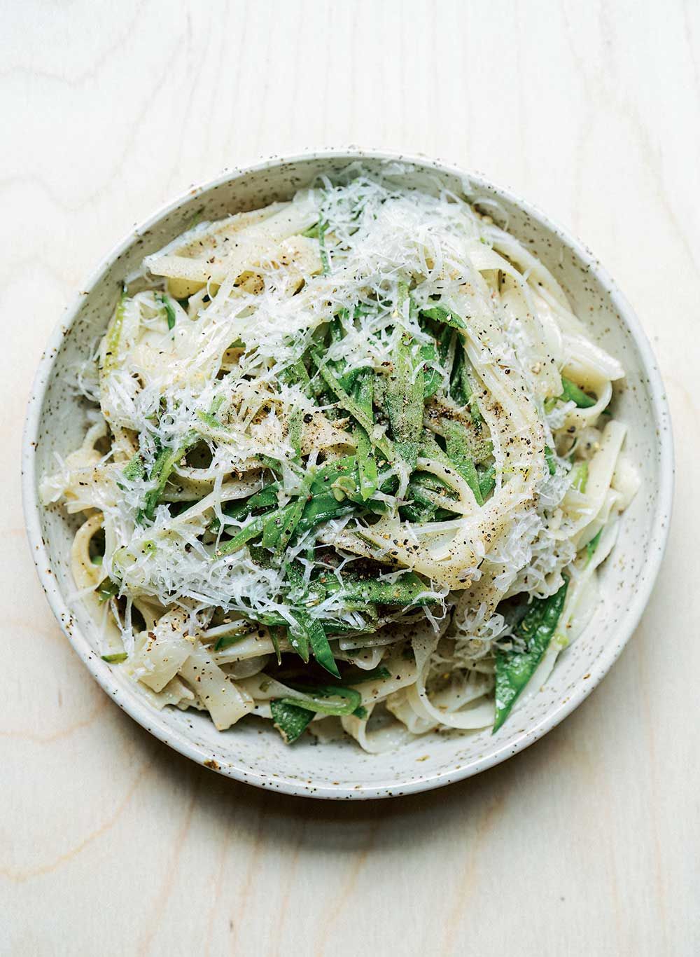 Plate with noodles, snow peas and grated cheese