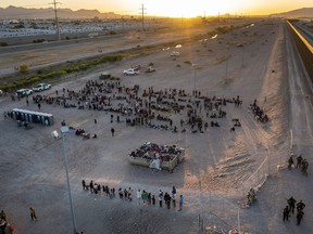 As the sun sets, migrants wait outside a gate in the border fence to enter into El Paso, Texas, to be processed by the Border Patrol, Thursday, May 11, 2023. Migrants rushed across the Mexico border, racing to enter the U.S. before pandemic-related asylum restrictions are lifted in a shift that threatens to put a historic strain on the nation's beleaguered immigration system.
