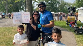 A family of four — mother, father, and two children — stand holding signs celebrating how they raised money for immunotherapy for glioblastoa, an agressive form of brain tumour