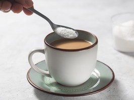 A person adding a spoonful of sweetener to a cup of tea.