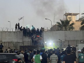 Protesters scale a wall at the Swedish Embassy in Baghdad Thursday, July 20, 2023. Protesters angered by the burning of a copy of the Quran stormed the embassy early Thursday, breaking into the compound and lighting a small fire.