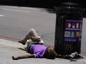 FILE - A homeless person lies on the sidewalk while holding a water bottle, Sunday, July 2, 2023, in downtown Los Angeles. Excessive heat warnings remain in place in many areas across the U.S. and are expected to last at least through Monday.