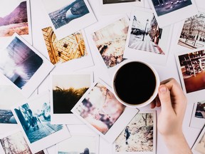 A hand holding cofee over a bunch of photographs.