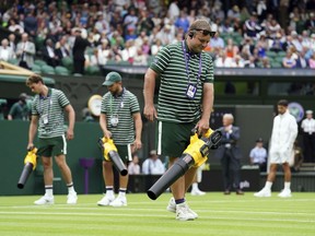 Members of the ground staff use leaf blowers to dry the court following a prolonged rain break in the men's singles match between Serbia's Novak Djokovic and Argentina's Pedro Cachin on day one of the Wimbledon tennis championships in London, Monday, July 3, 2023.
