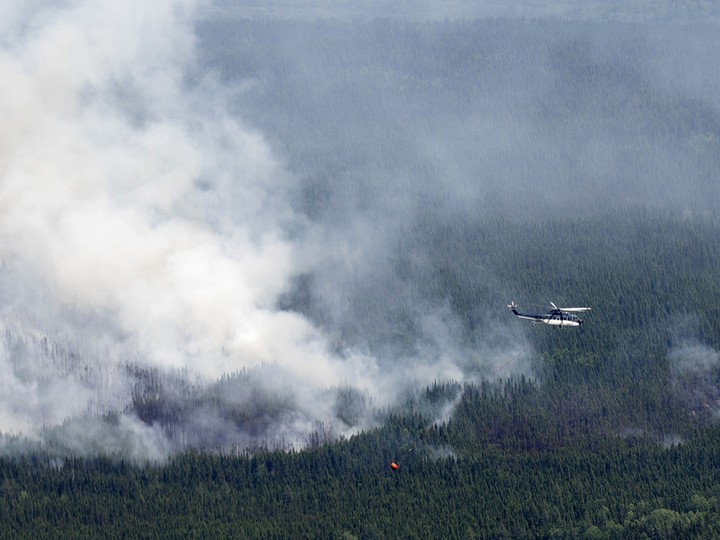  A helicopter carrying a water basket flies past a wildfire near Lebel-sur-Quevillon, Quebec.