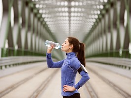 Young runner resting, drinking water on green steel bridge