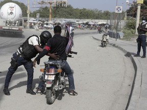 A police officer pats down a motorcyclist at a checkpoint in Port-au-Prince, Haiti, Saturday, July 1, 2023.