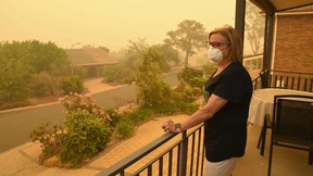 Woman wearing a mask standing on a balcony surrounded by a haze of smoke.