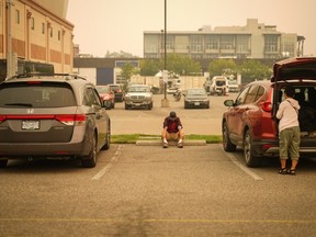 A man sits in the parking lot outside an evacuation centre for those forced from their homes due to wildfires, in Kelowna, B.C., Saturday, Aug. 19, 2023.
