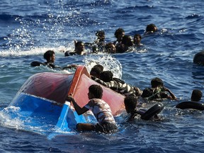 Migrants swim next to their overturned wooden boat during a rescue operation south of the Italy's Lampedusa island.