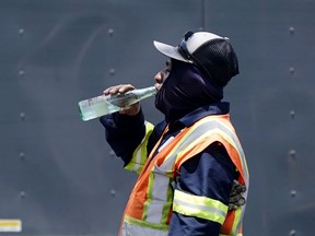 FILE - Standing in the mid-afternoon heat, a worker takes a break to drink during a parking lot asphalt resurfacing job in Richardson, Texas, June 20, 2023. While unrelenting heat set in across Texas this summer, opponents of a sweeping new law targeting local regulations took to the airwaves and internet with an alarming message: outdoor workers would be banned from taking water breaks. Workers would die, experts and advocates said, with high temperatures topping 100 degrees Fahrenheit (38 degrees Celsius) and staying there for much of the past two months.