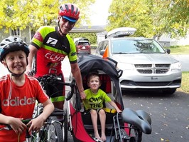 Bernard McNeil, Noah and Malik Trépanier. Grandfather stands with grandsons wearing cycling gear.