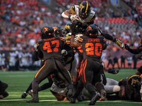 Hamilton Tiger-Cats' James Butler jumps over BC Lions' Sione Teuhema (47) and Boseko Lokombo (20) to score a touchdown during first half CFL football action in Vancouver on Saturday, August 26, 2023.