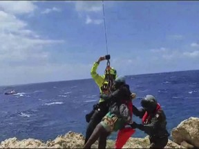In this picture taken from video distributed on Sunday, Aug. 6, 2023 by the Italian Alpine Rescue squads, a migrant stranded on a rocky reef on the tiny Italian southern island of Lampedusa, Sicily is pluck to safety by helicopter. Dozens of migrants were dramatically rescued by Italy as they foundered in the sea or clung to a rocky reef Sunday after three boats launched by smugglers from northern Africa shipwrecked in rough waters in separate incidents over the weekend
