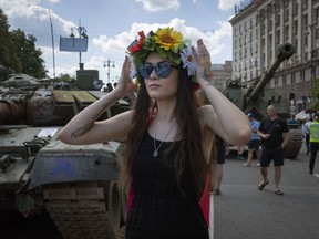 A woman wears a flower hair garland as people look at a large column of burnt out and captured Russian tanks and infantry carriers which have been on display on the central Khreshchatyk boulevard as Ukrainians mark Independence Day, in Kyiv, Ukraine, Thursday, Aug. 24, 2023.