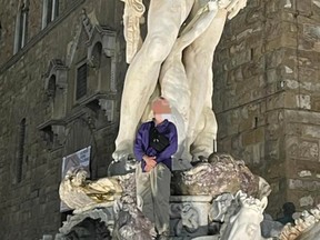 A tourist poses for a photo on Florence's Fountain of Neptune.