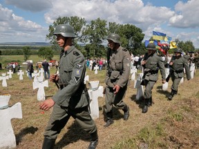 Ukrainians dressed in SS Galicia Division uniforms march past graves.