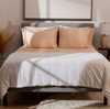 A perfectly made bed with grey padded headboard, pale orange pillows and white weight blanket laid on top.