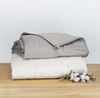 A neatly folded stack of linens, consisting of one thin weighted blanket and one blanket cover.