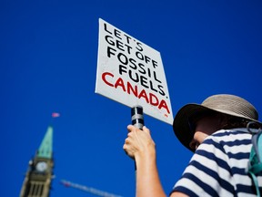 A protester holds a sign that says Let's get off fossil fuels Canada