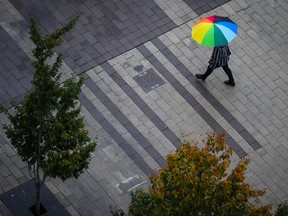 A pedestrian carries an umbrella as light rain falls in Surrey, B.C., on Friday, Oct. 21, 2022. Environment Canada has issued wind warnings for much of British Columbia's coast ahead of a storm expected Monday.