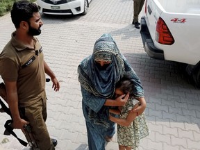Police officers escort a relative and a child of a couple wanted by British police in connection with last month's death of their 10-year-old daughter on the outskirts of London, to appear them in a court in Jhelum, about 175 kilometres (110 miles) northwest of Lahore in central Pakistan, Tuesday, Sept. 12, 2023. A Pakistani court ordered the five siblings of a 10-year-old girl who was found dead at her British home put in the custody of a children's protection center after they were recovered following a notice from Interpol. The police are continuing their search for the girl's father and stepmother in connection with her death.