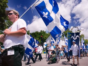People carry Quebec flags as they parade down a street.