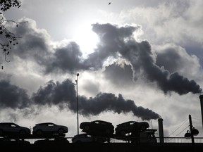 FILE - Smoke rises from a factory as a truck loaded with cars crosses a bridge in Paris, on Nov. 30, 2018. President Emmanuel Macron is to unveil France's approach and means to meet its climate-related commitments within the next seven years as a special government meeting is taking place on Monday Sept. 25, 2023.