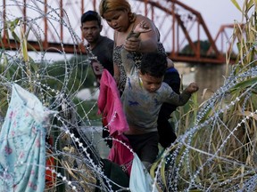 Migrants climb over concertina wire after they crossed the Rio Grande and entered the U.S. from Mexico, Saturday, Sept. 23, 2023, in Eagle Pass, Texas.