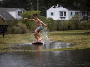 Zach Wright, 12, skimboards in floodwaters from the Lafayette River in the Larchmont Neighborhood of Norfolk, Va., Friday, Sept. 22, 2023, as Tropical Storm Ophelia approaches.