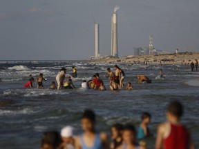 Palestinians walk on the beach close to the divide with Israel in the background, near Gaza City on September 12, 2014.