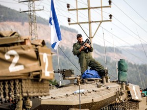 An Israeli army soldier stands holding shells atop the turret of a Merkava battle tank as a column of tanks is amassed in upper Galilee northern Israel near the border with Lebanon on October 11, 2023.