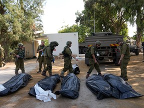 Israeli soldiers stand next to the bodies of Israelis killed by Hamas fighters in the Kfar Azza kibbutz in southern Israel, about five kilometres east of Gaza, on Oct. 10, 2023.