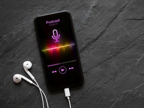 Earphones and mobile phone with podcast app on screen on black background.