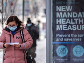 A woman walks by a bus stop with a poster explaining "new mandatory health measures."