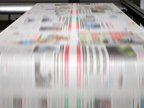 File photo of a printing press running a long roll of paper over its rollers at high speed.