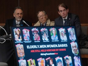 Three men with a poster covered with hostages in front of them.