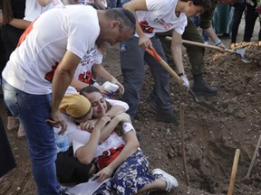 Two women embrace as people dig a grave