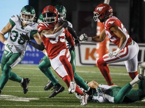 Saskatchewan Roughriders defensive back Jayden Dalke, left, looks on as Calgary Stampeders running back Ka'Deem Carey, centre, escapes the grasp of linebacker Micah Teitz during second half CFL football action in Calgary, Friday, Oct. 13, 2023.THE CANADIAN PRESS/Jeff McIntosh