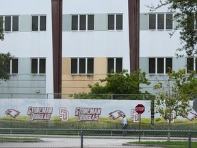 FILE - A security agent walks alongside a barrier surrounding Marjory Stoneman Douglas High School, July 5, 2023, in Parkland, Fla. Florida lawmakers and others on Saturday, Oct. 14, toured the school's 1200 Building, where a former student shot 17 people to death and wounded 17 others on Valentine's Day in 2018. The local school district has announced the 1200 Building will be demolished during the summer of 2024.