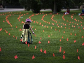Margot King, 4, touches an orange flag, representing children who died while attending Indian Residential Schools in Canada, placed in the grass at Major's Hill Park in Ottawa, on Canada Day, Thursday, July 1, 2021. A First Nation in northwestern Ontario says it has found 22 areas where historic human remains may be buried at the site of a former residential school.