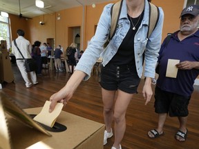 A man, right, waits as a woman drops her ballot into a box a polling place in Redfern as Australians cast their final votes in Sydney, Saturday, Oct. 14, 2023, in their first referendum in a generation that aims to tackle Indigenous disadvantage by enshrining in the constitution a new advocacy committee. Australia will look for new ways to lift Indigenous living standards after voters soundly rejected a proposal to create a new advocacy committee, the deputy prime minister said on Sunday, Oct. 15.