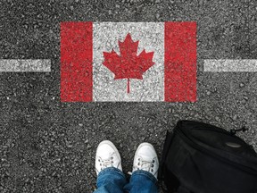 Looking down at shoes while standing on asphalt next to flag of Canada at the border..