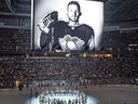 The Pittsburgh Penguins and Anaheim Ducks gather at center ice, before an NHL hockey game in Pittsburgh, Monday, Oct. 30, 2023, to honor former Penguin player Adam Johnson, shown on scoreboard, who died in while playing in an English hockey league game.