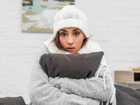 A woman bundled up on a couch in a cold house.