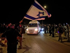 A man waves an Israeli flag as a vehicle carrying hostages released by Hamas passes by.