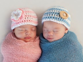 A baby wrapped in a pink blanket next to a baby in a blue blanket.